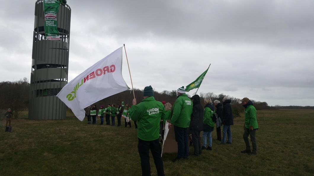 Een groep GroenLinksers staat met vlaggen bij de toren van Vliegveld Twente