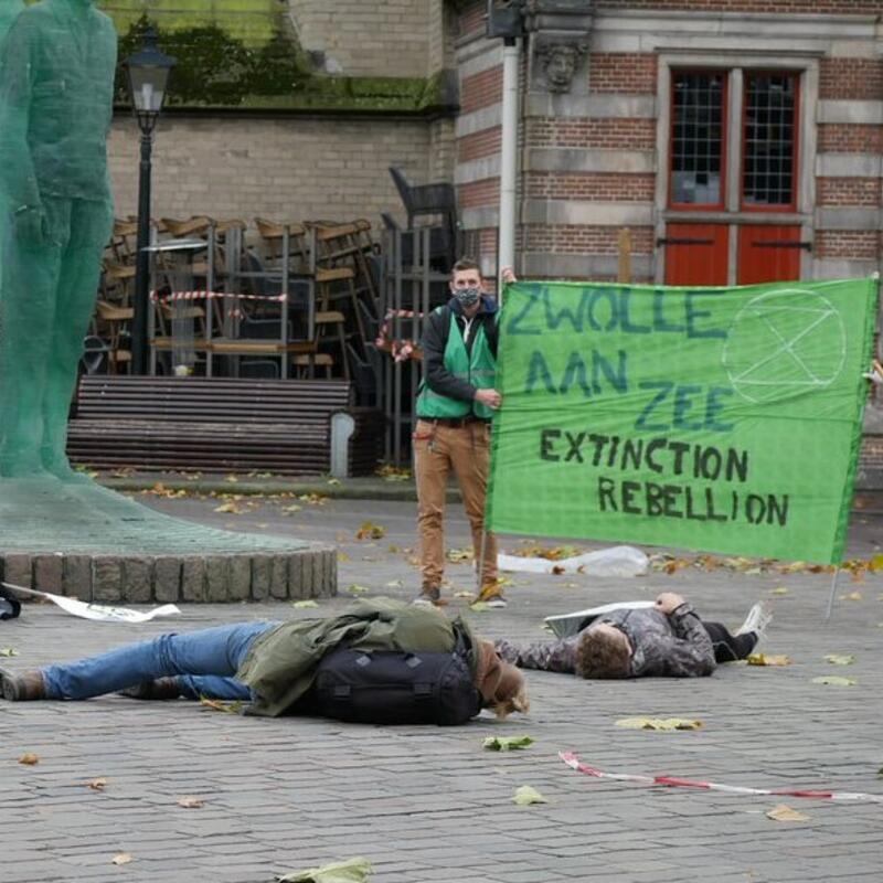 Rob in actie bij XR. Hij staat naast de Engel op de Grote Markt in Zwolle met een spandoek. Voor hem liggen actievoerders op de grond.