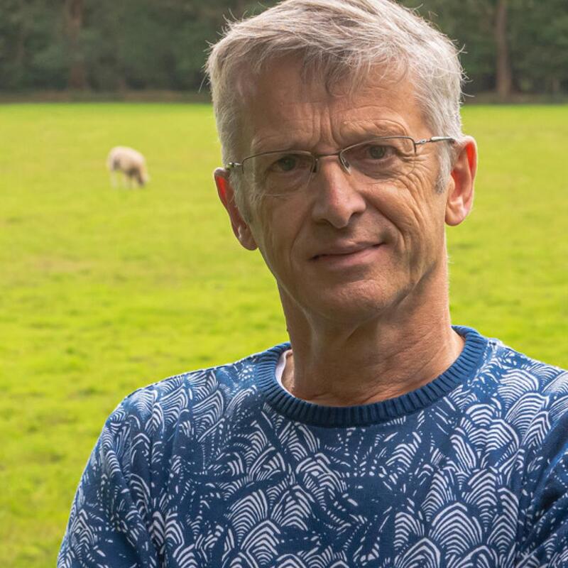 Henk Nijmeijer. Hij heeft een blauw shirt aan. Op de achtergrond zie je een weiland.